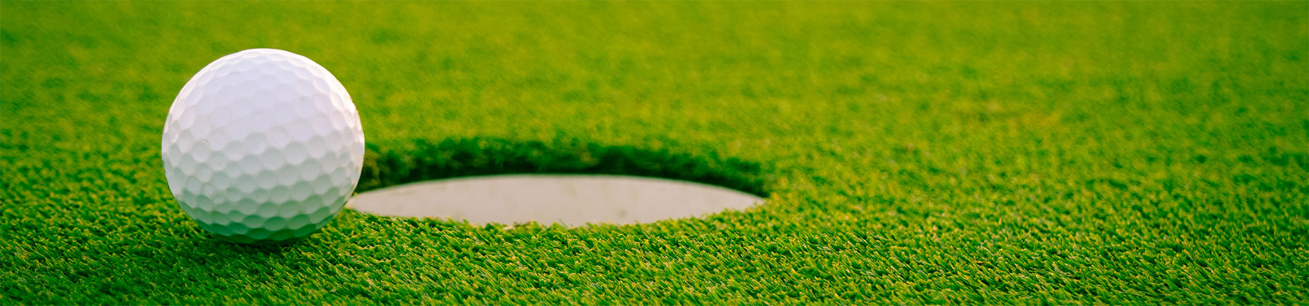 A golf ball resting near a hole on a green turf surface, highlighting the game's precision.