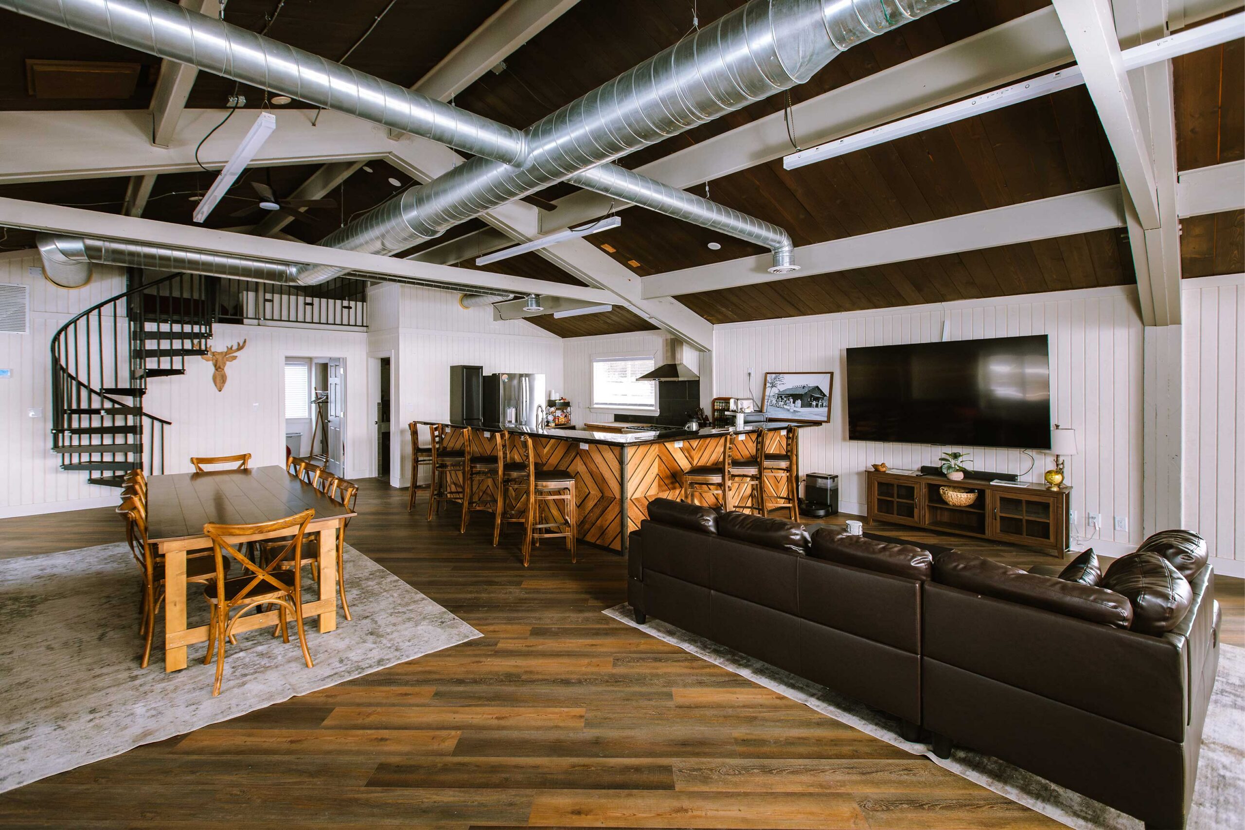 Spacious modern living area featuring a wooden dining table, bar, and leather couch with a spiral staircase.