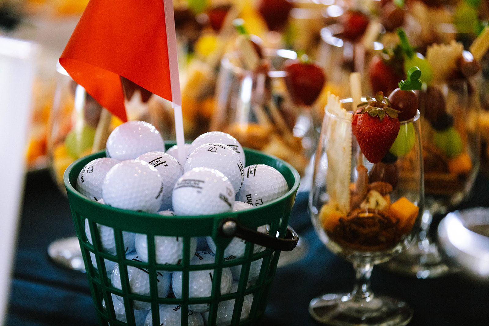 A green basket filled with golf balls and a small red flag, surrounded by fruit and dessert displays.