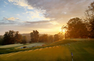 Sunrise over a golf course with trees and rolling hills, casting a warm glow on the landscape.