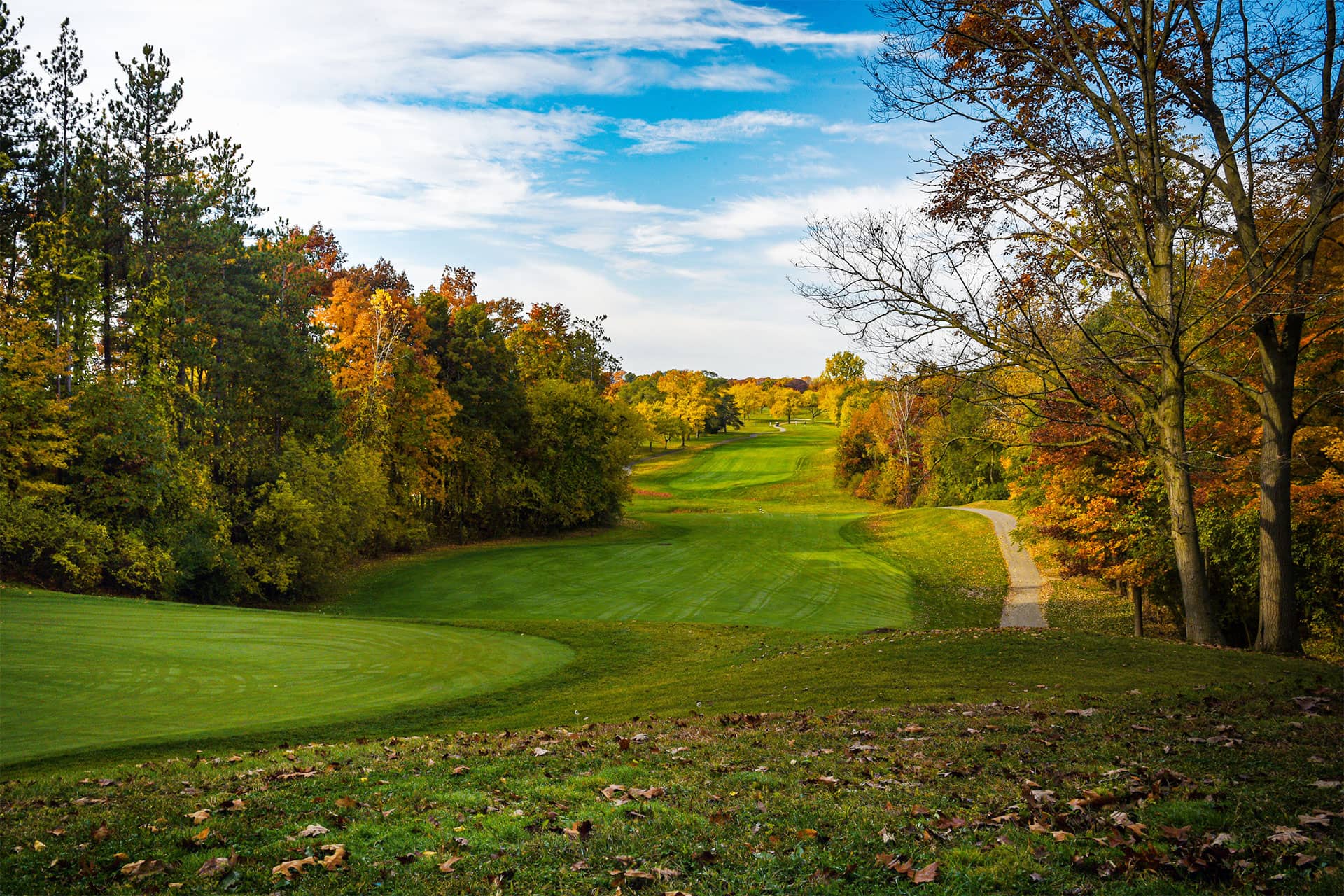 A scenic view of a golf course surrounded by autumn foliage and a clear blue sky.