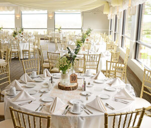 Elegant banquet setup with round tables, white linens, and floral centerpieces in a bright venue.