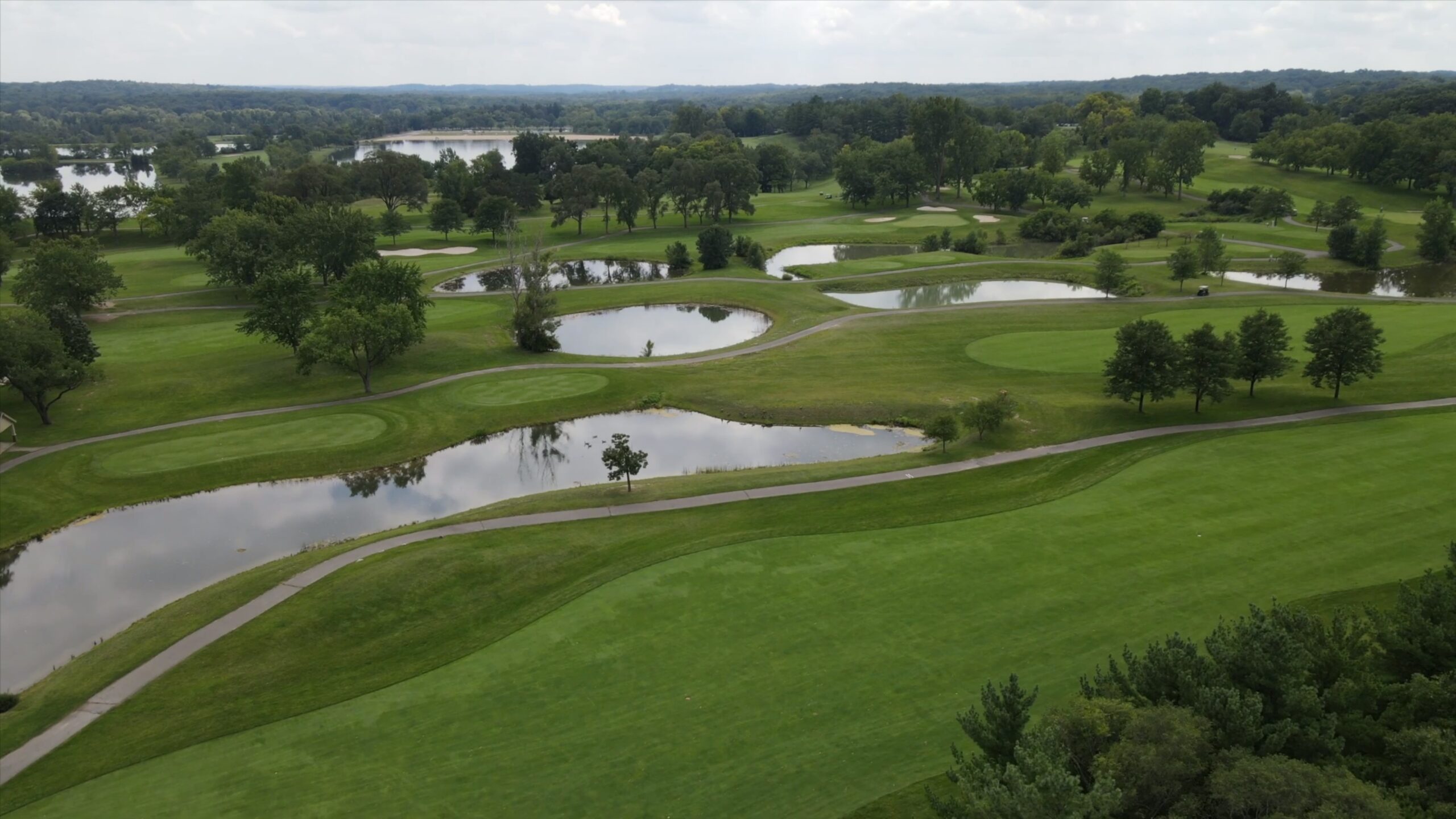 Aerial view of a lush green golf course with ponds and trees, showcasing a serene landscape at Mystic Creek.