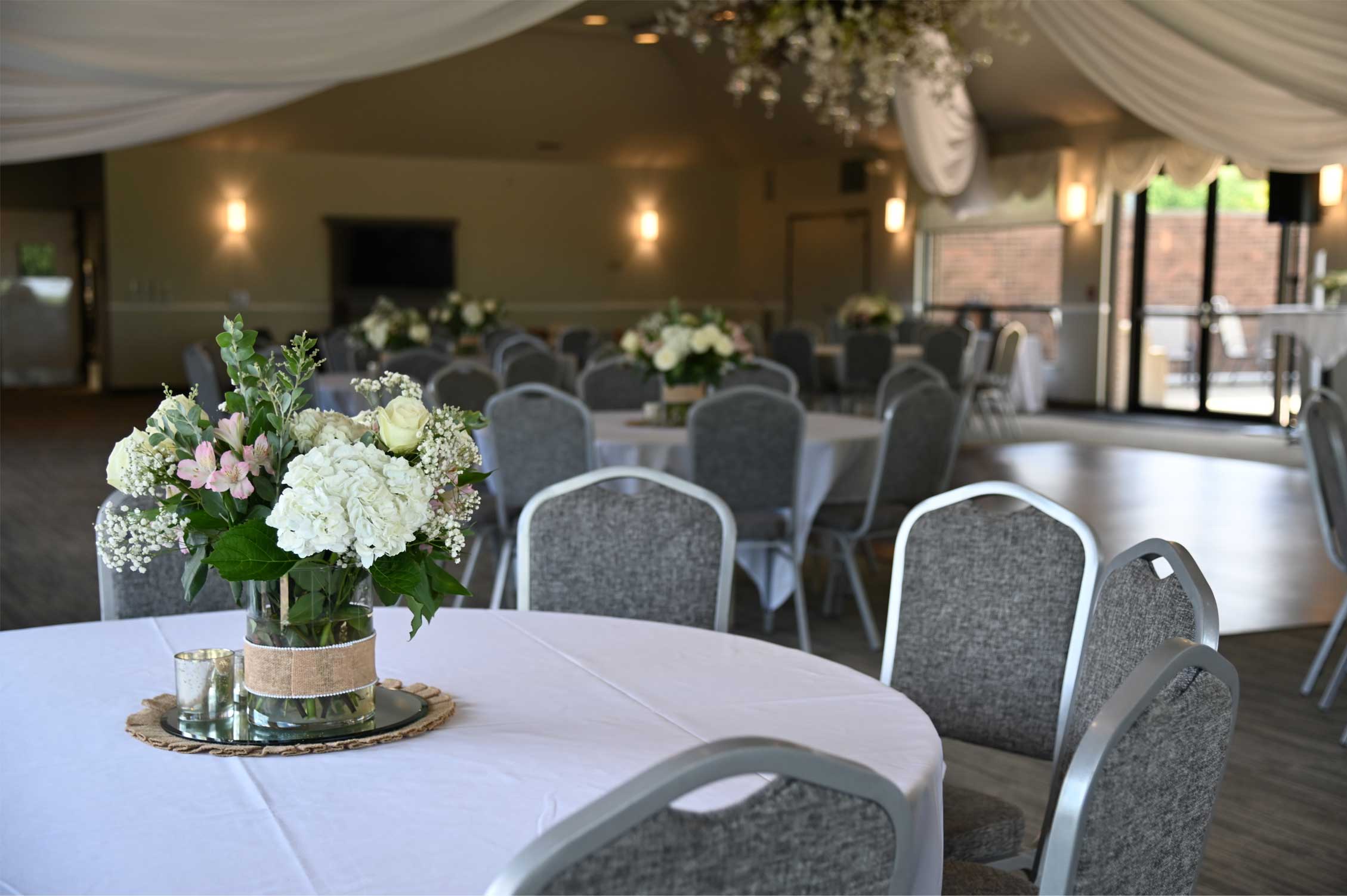 A beautifully arranged table with a floral centerpiece in a spacious event venue, featuring gray chairs and soft lighting.
