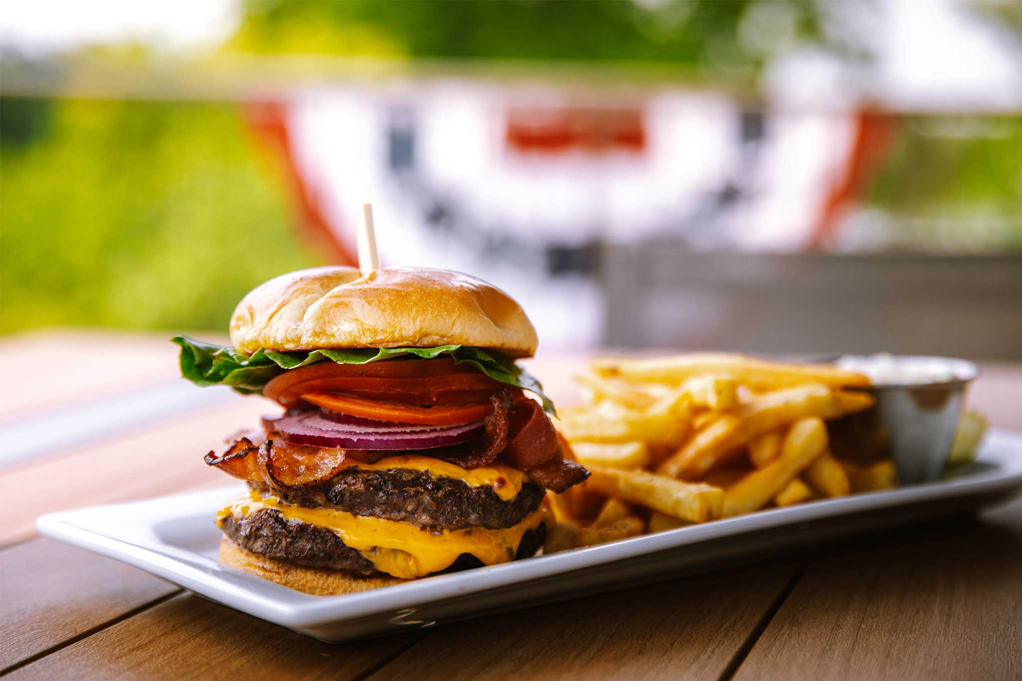 A stacked burger with lettuce, tomato, onion, bacon, and cheese served with fries on a plate.