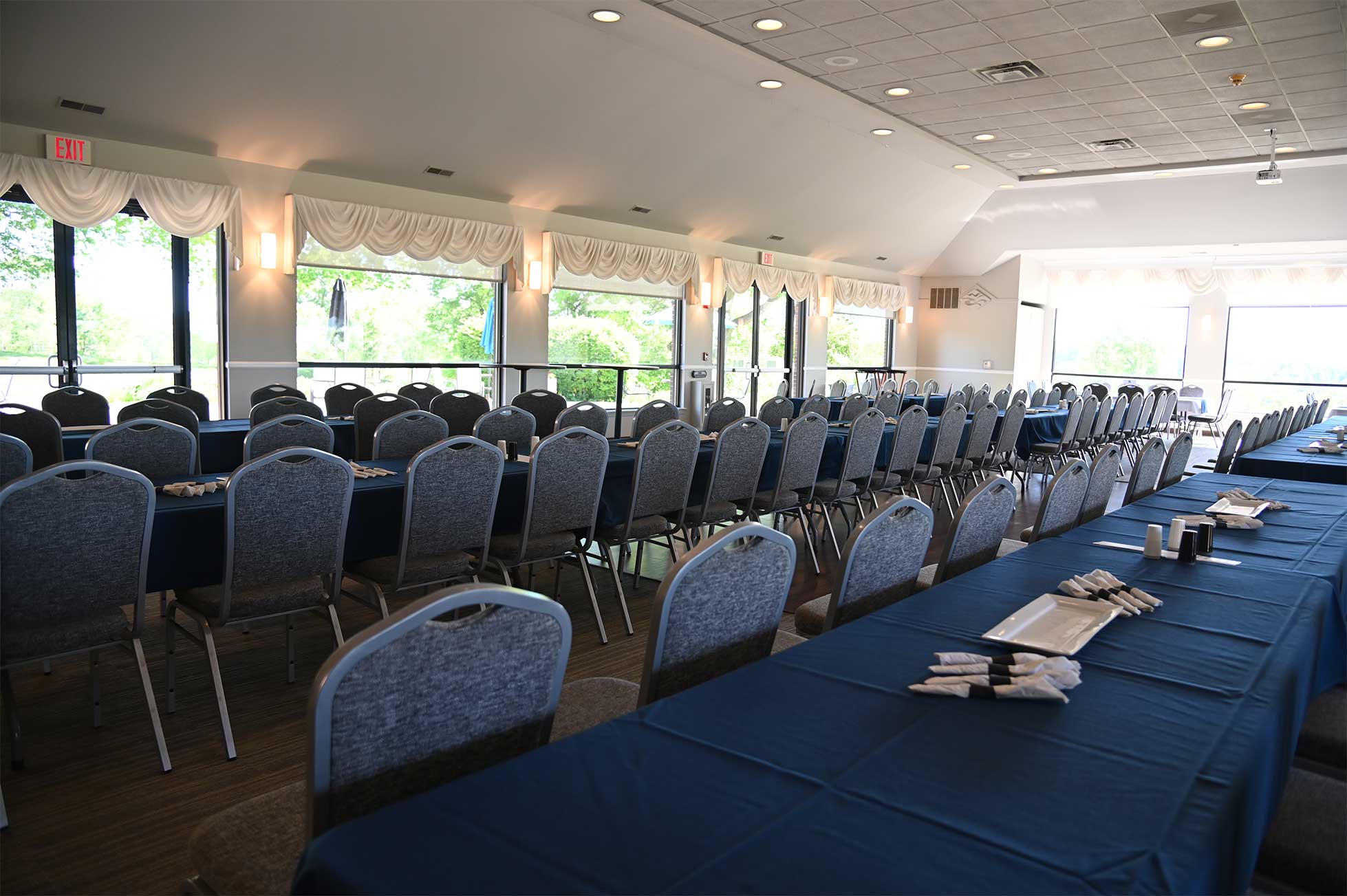 Spacious banquet room with rows of tables set with blue tablecloths and neatly arranged utensils.